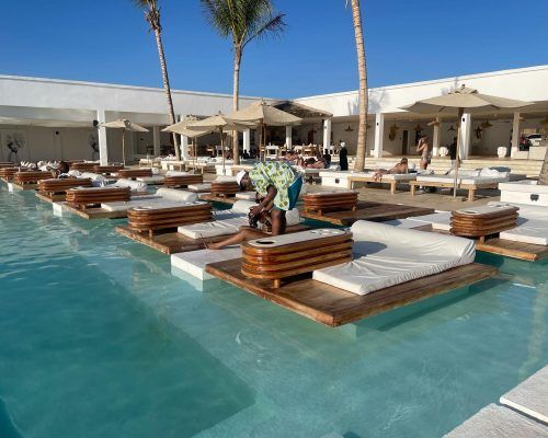 Guests lounging on floating sunbeds at the beach club pool under a clear Zanzibar sky