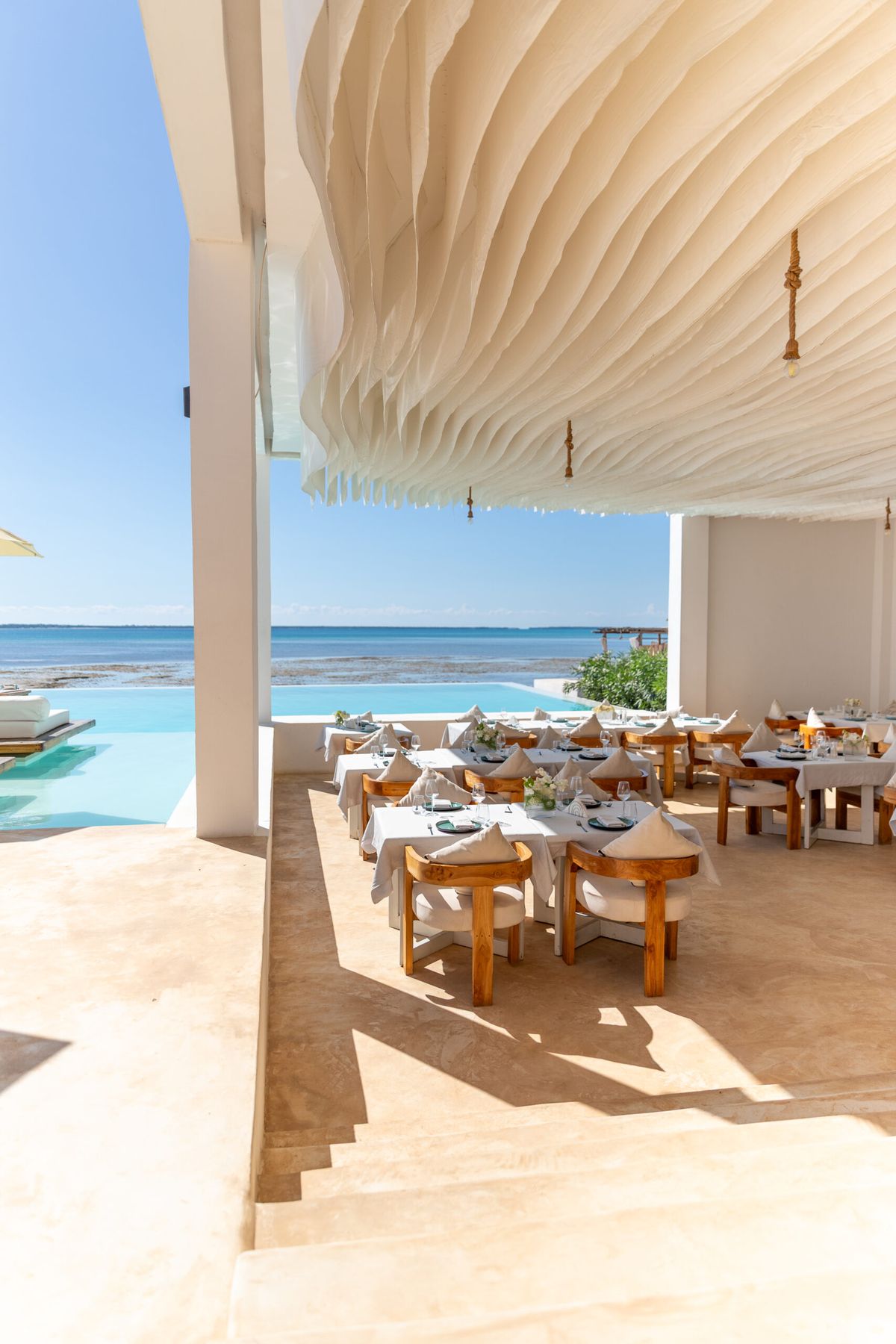 Dining tables beneath the sculpted ceiling with the infinity pool and ocean beyond