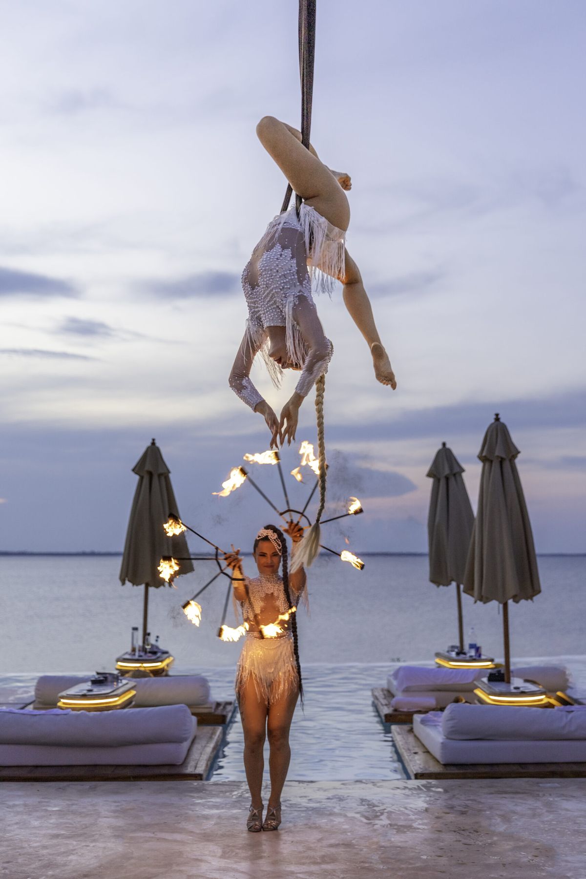 Aerial and fire performers at dusk over the beach club sunbeds